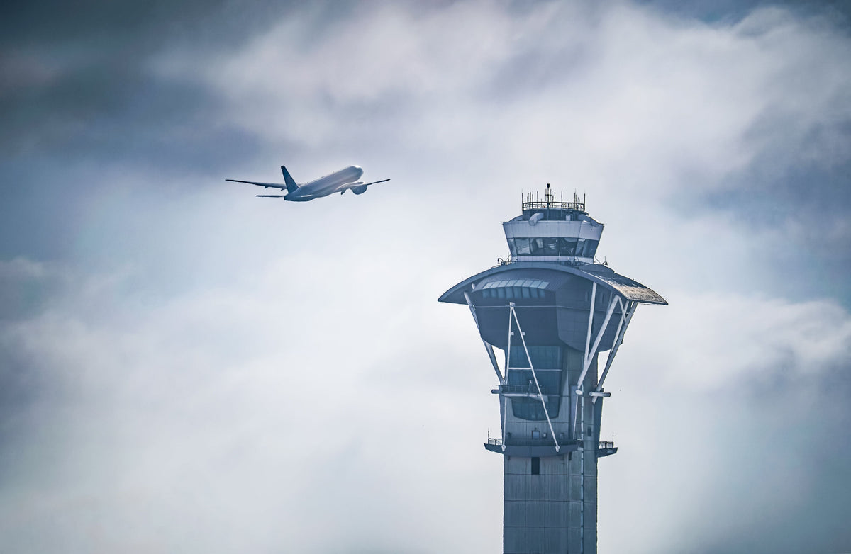 Image of commercial airplane taking off in distance with air traffic control tower in foreground. Image by SolyMoses@pexels.com